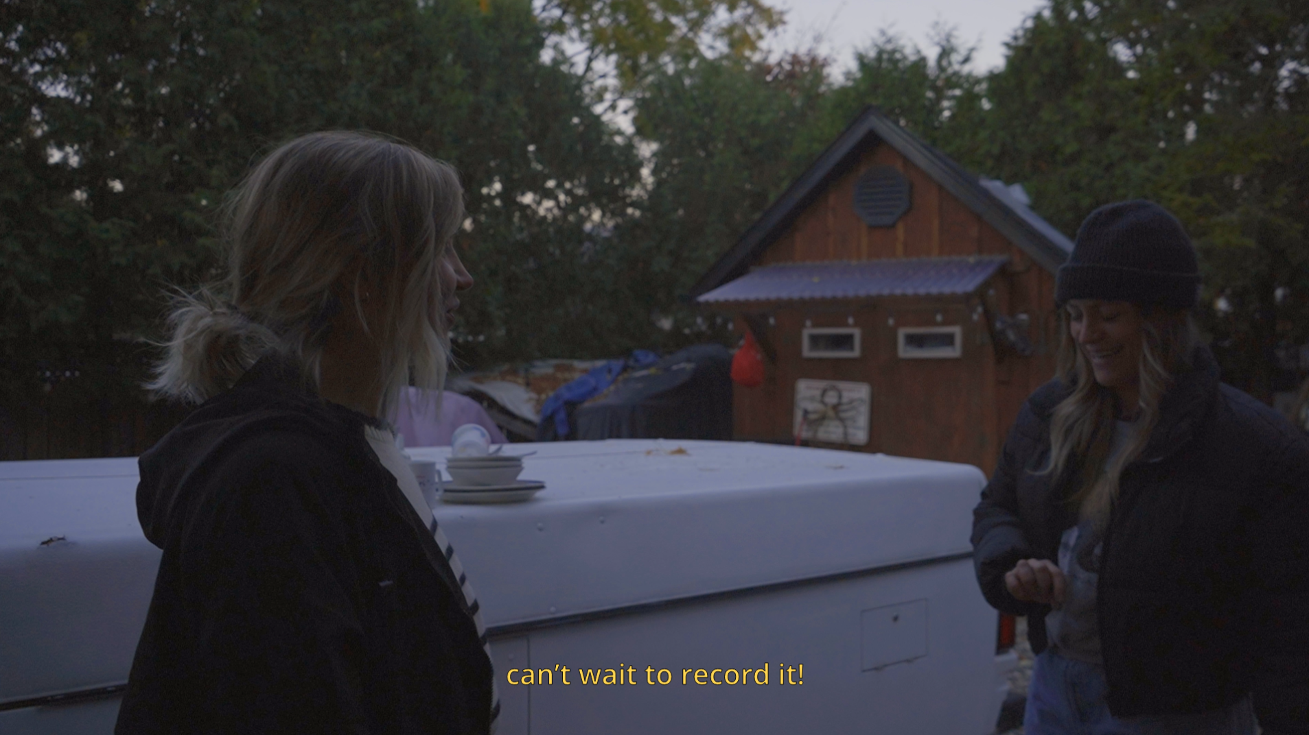 Two women laughing in a backyard, one saying 'can’t wait to record it!' as they prepare for a project