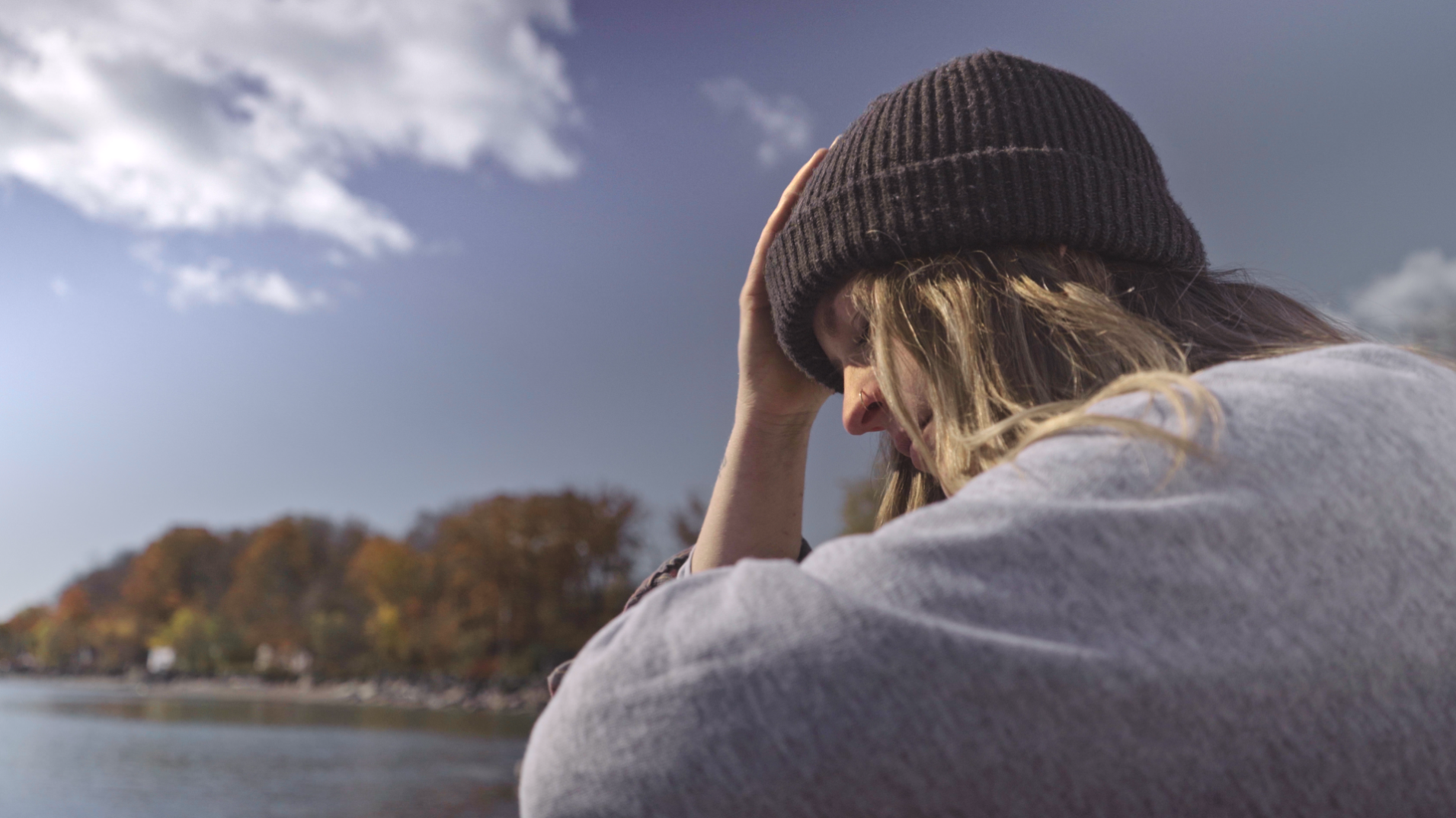 Rachel looking down thoughtfully beside a lake on a crisp autumn day