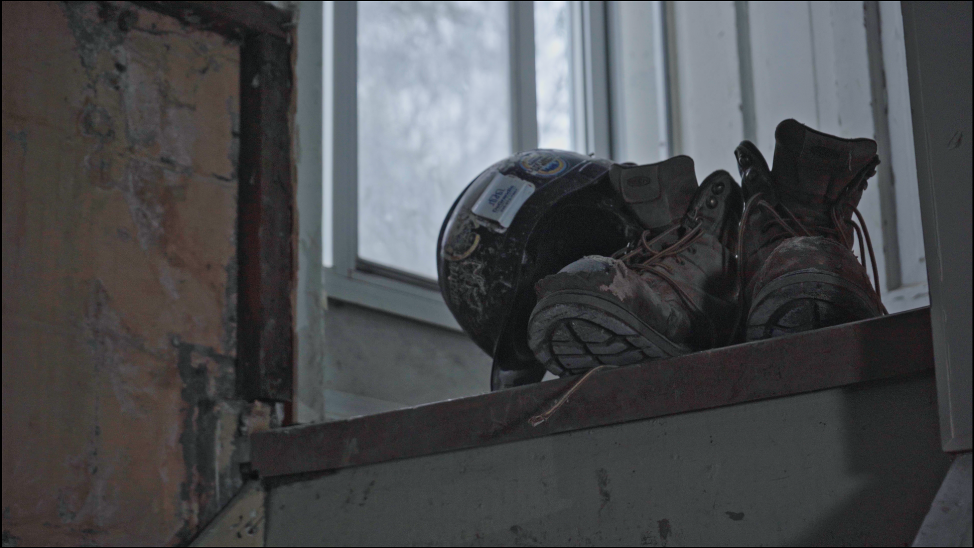 Worn work boots and a hard hat resting on a dusty ledge in a partially renovated space