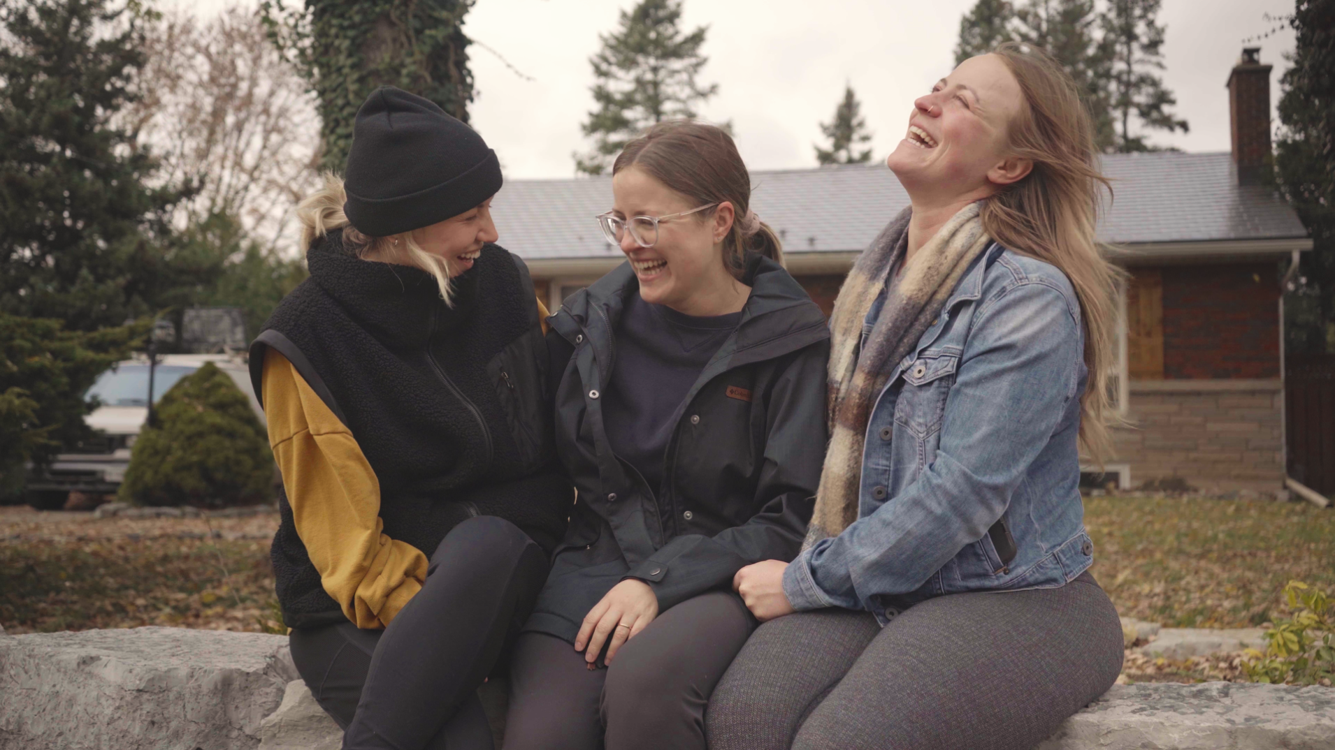 Three women sitting outside a home, laughing together in a candid moment